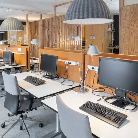 Kontorsmiljö med flera skrivbord i rad, utrustade med datorskärmar, tangentbord och skrivbordslampor i ett öppet kontorslandskap