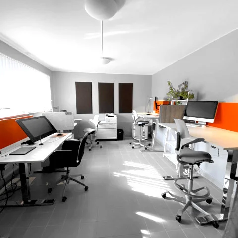 Modernt kontorsrum med flera arbetsstationer, kontorsstolar och stora fönster som släpper in dagsljus