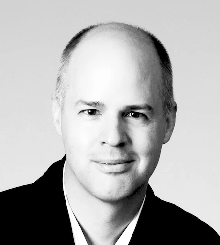 Svartvitt porträtt av Klas Hermodsson med skalligt huvud och neutralt ansiktsuttryck, iklädd mörk kavaj.